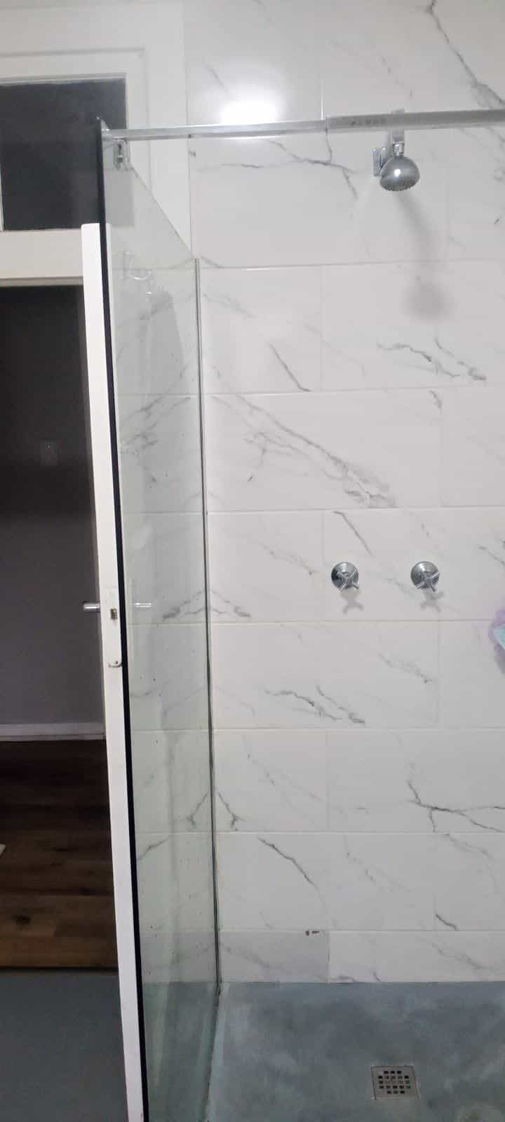 Walk-in shower with glass door and full-height marble-look tiling