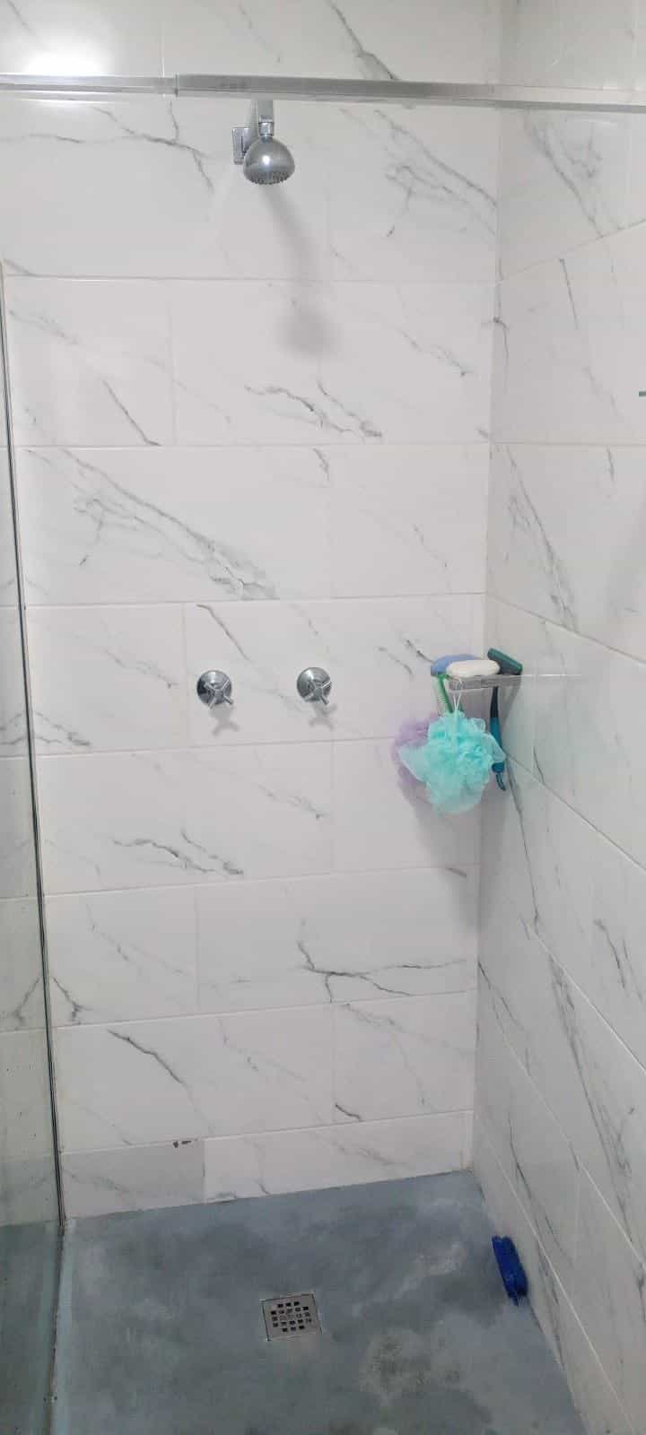 Tiled shower wall with chrome mixer taps and corner shelf