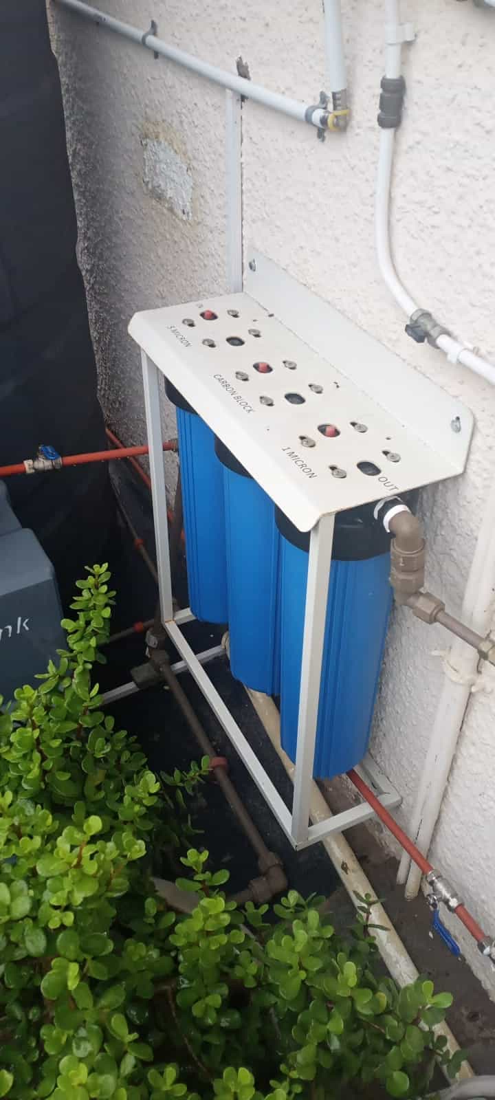 Whole-house 3-stage water filtration by Elite Home Finishes: 5-micron, carbon block and 1-micron filters on a wall rack