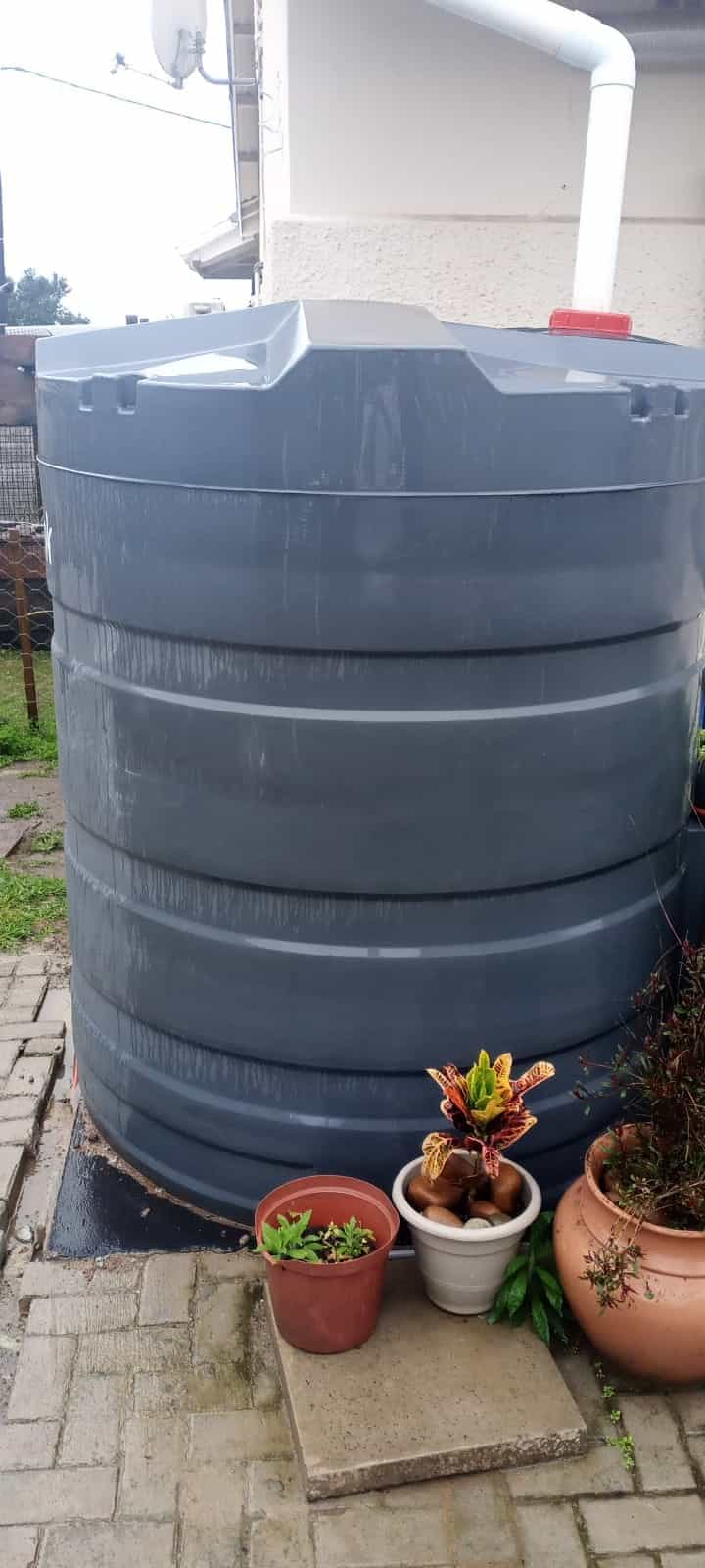 Charcoal RotoTank rainwater tank on a level base, connected to the roof downpipe