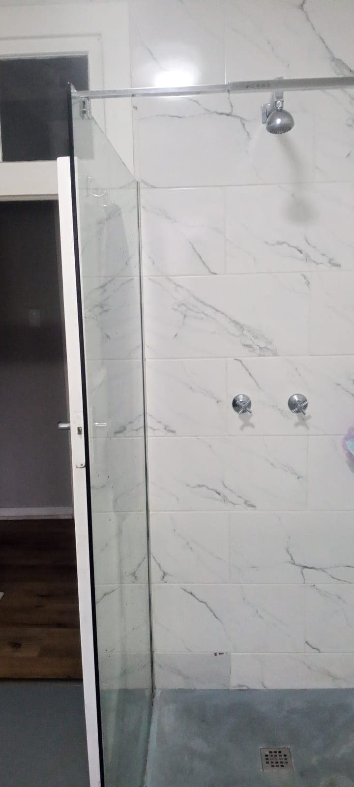Walk-in shower with glass door and full-height marble-look tiling