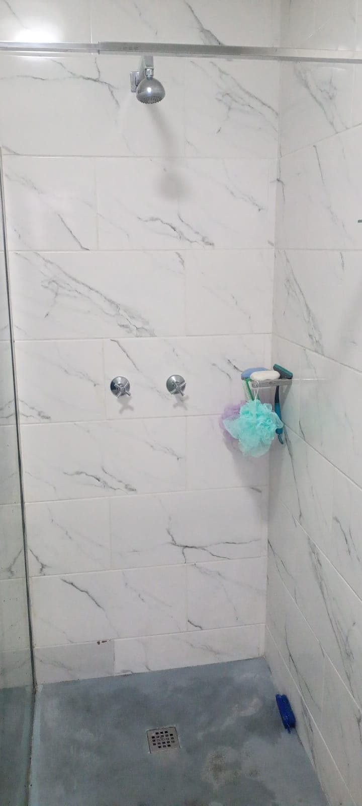 Tiled shower wall with chrome mixer taps and corner shelf