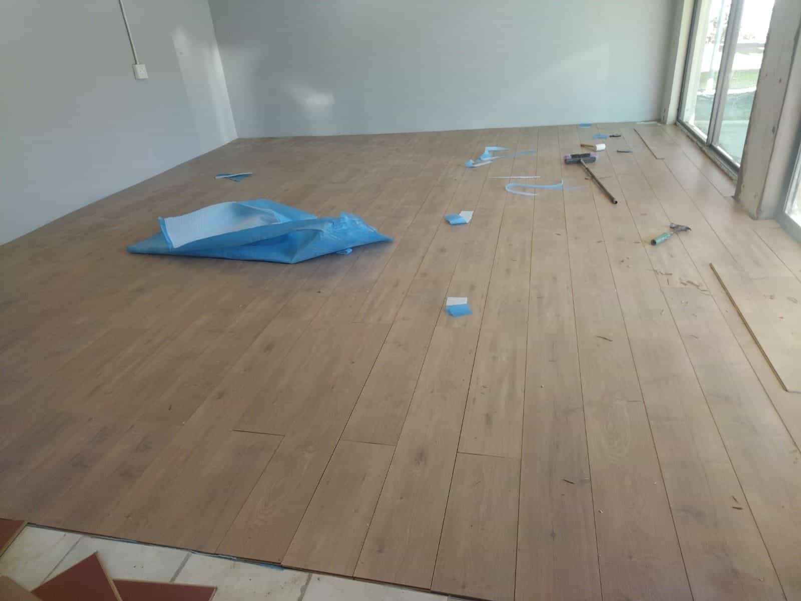 Laminate plank flooring being laid through an open-plan room by our team
