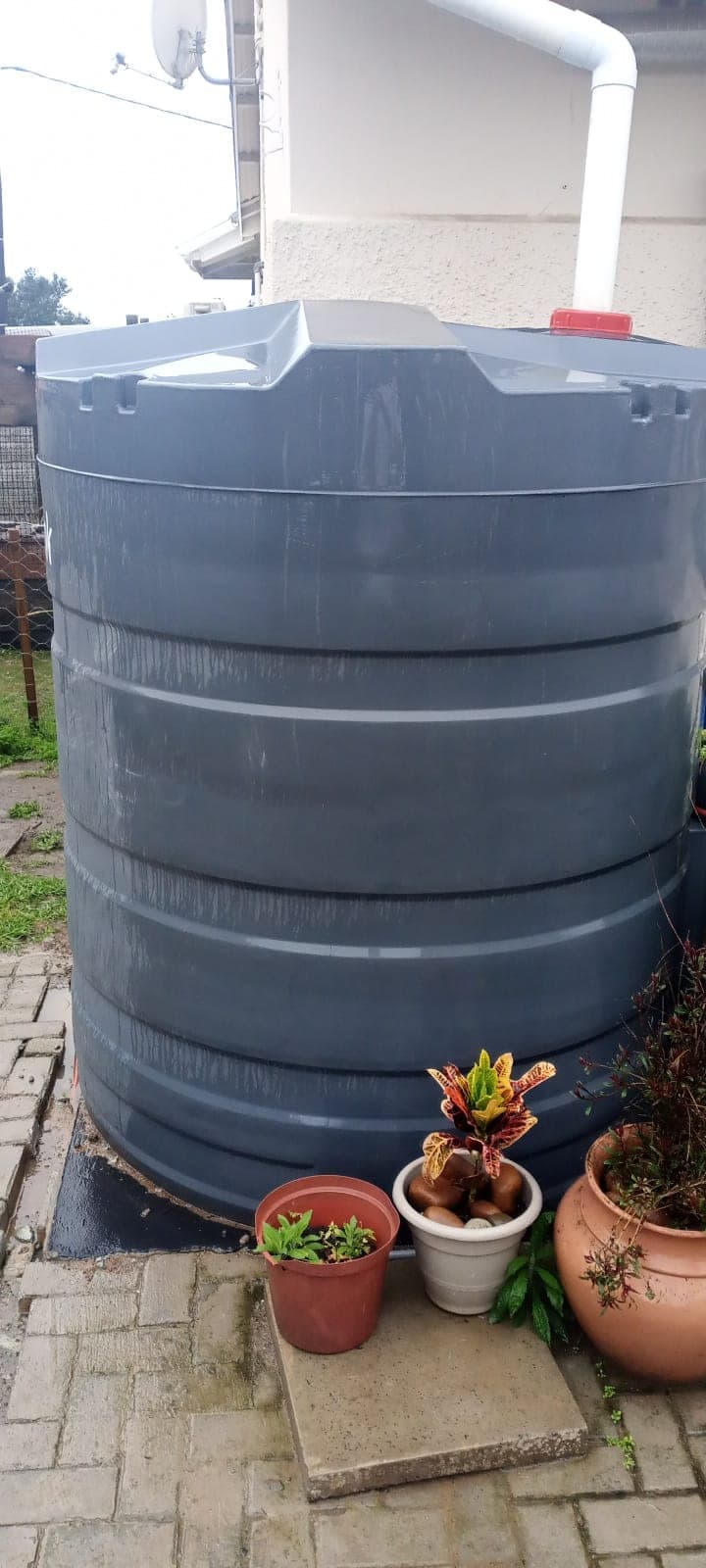 Charcoal RotoTank rainwater tank on a level base, connected to the roof downpipe